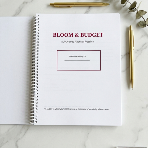 Open notebook titled 'Bloom & Budget' on a marble surface with a pen and decorative elements.