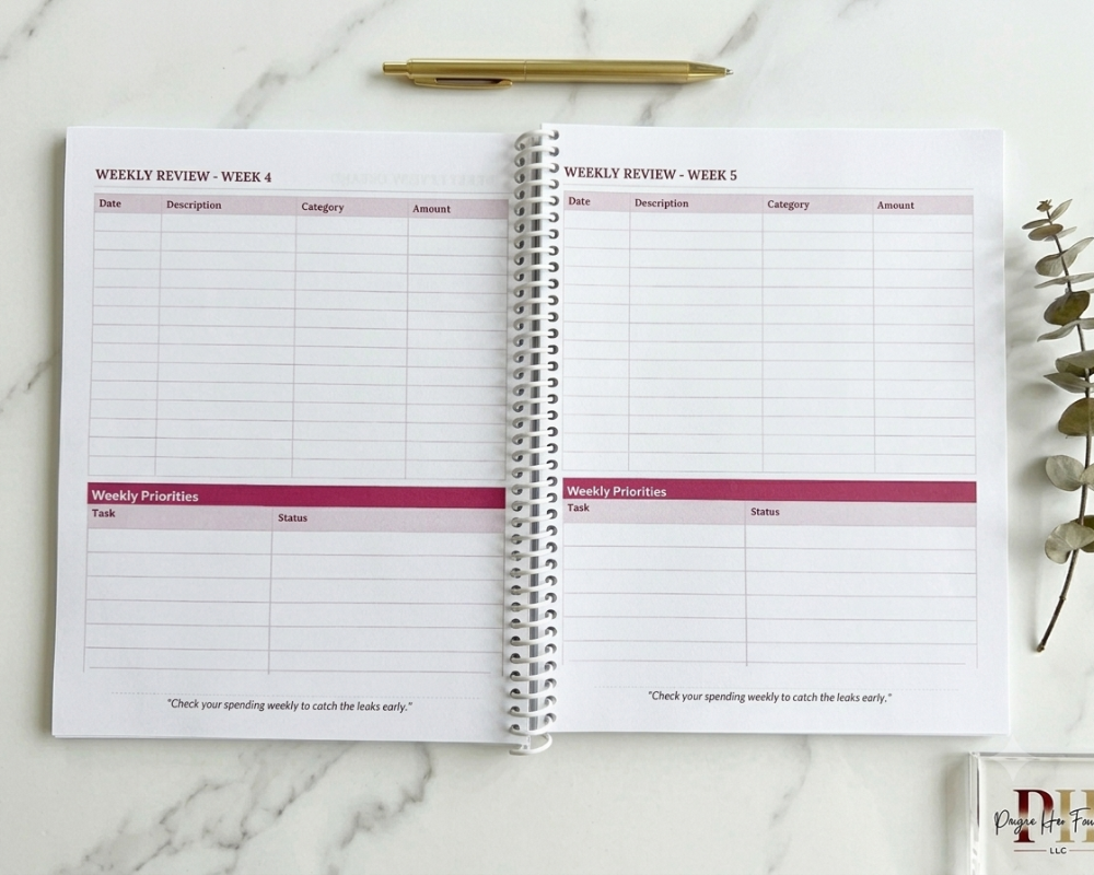 Open planner with weekly review pages on a marble surface, featuring a pen and plant.