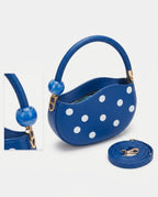 Blue handbag with white polka dots and matching strap on a light gray background
