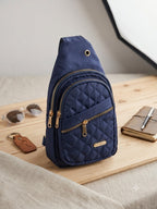 Navy blue quilted sling bag on a wooden surface with sunglasses, keychain, and notebook.