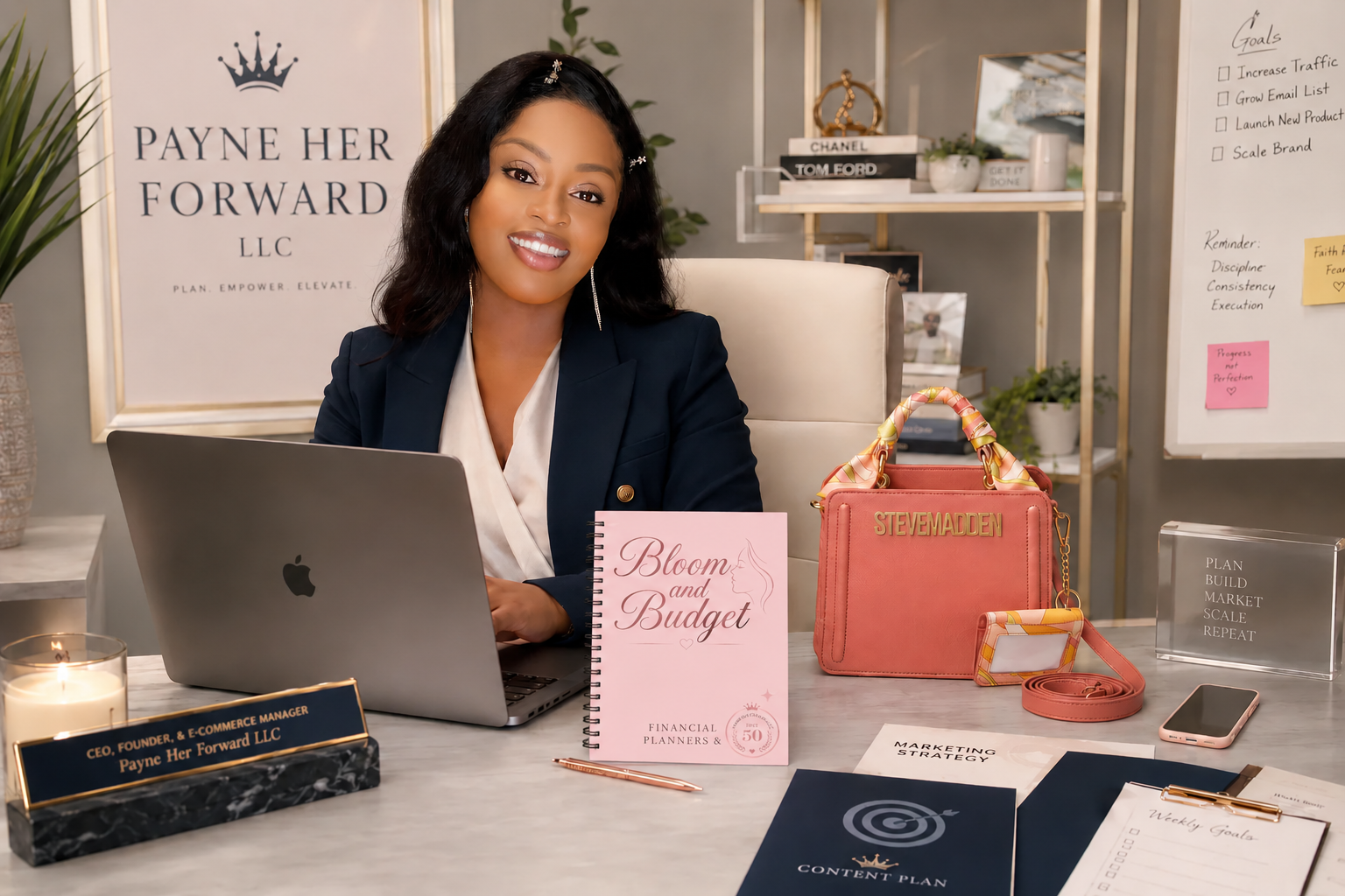 Woman sitting at a desk with a laptop, notebook, and a pink bag in an office setting.