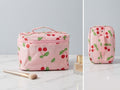 Pink cosmetic bag with cherry pattern on a light gray background
