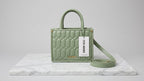 Green handbag with a visible brand label on a marble surface