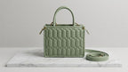 Green quilted handbag on a marble surface with a light gray background