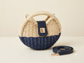 Woven handbag with navy bottom and cream top, accompanied by a matching strap on a light background
