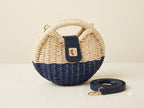 Woven handbag with navy bottom and cream top, accompanied by a matching strap on a light background
