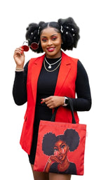 Woman holding a red tote bag with a graphic of a woman with styled hair, wearing a red vest and black top outdoors.